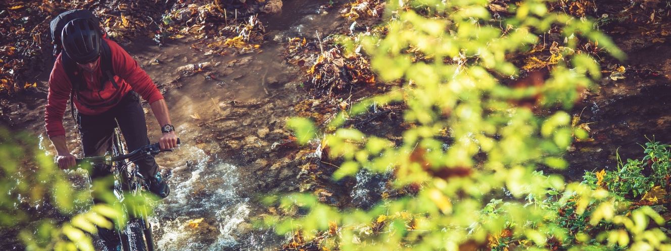 Man riding mountain bike through small creek
